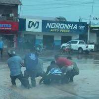 Seis homens tentam salvar uma moto sugada por um buraco durante uma forte chuva