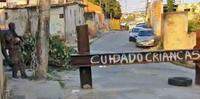 Reprodução / Policial inspeciona rua fechada por barricada, onde escreveram 'Cuidado: crianças' — Foto: Reprodução/G1 / TV Globo