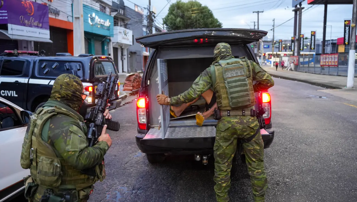 A imagem em destaque mostra policiais civis colocando um dos presos dentro da viatura.