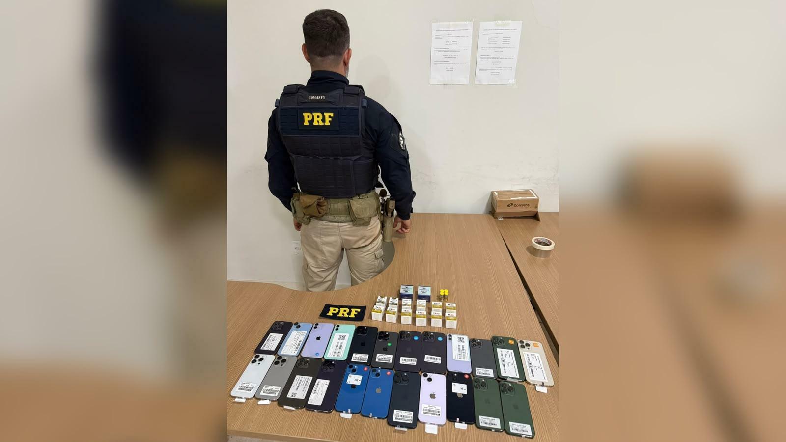 A imagem em destaque mostra um policial rodoviário federal próximo aos objetos apreendidos.