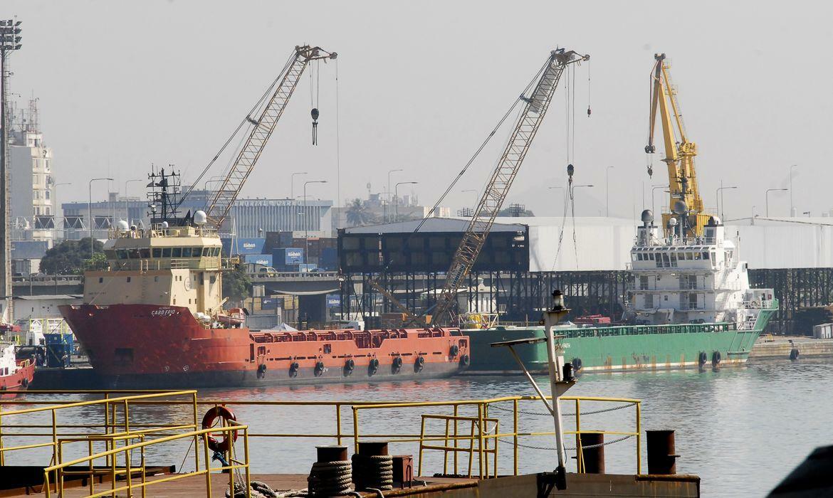 A imagem mostra navios atracados no Porto do Rio de Janeiro, com guindastes e embarcações de apoio de fundo