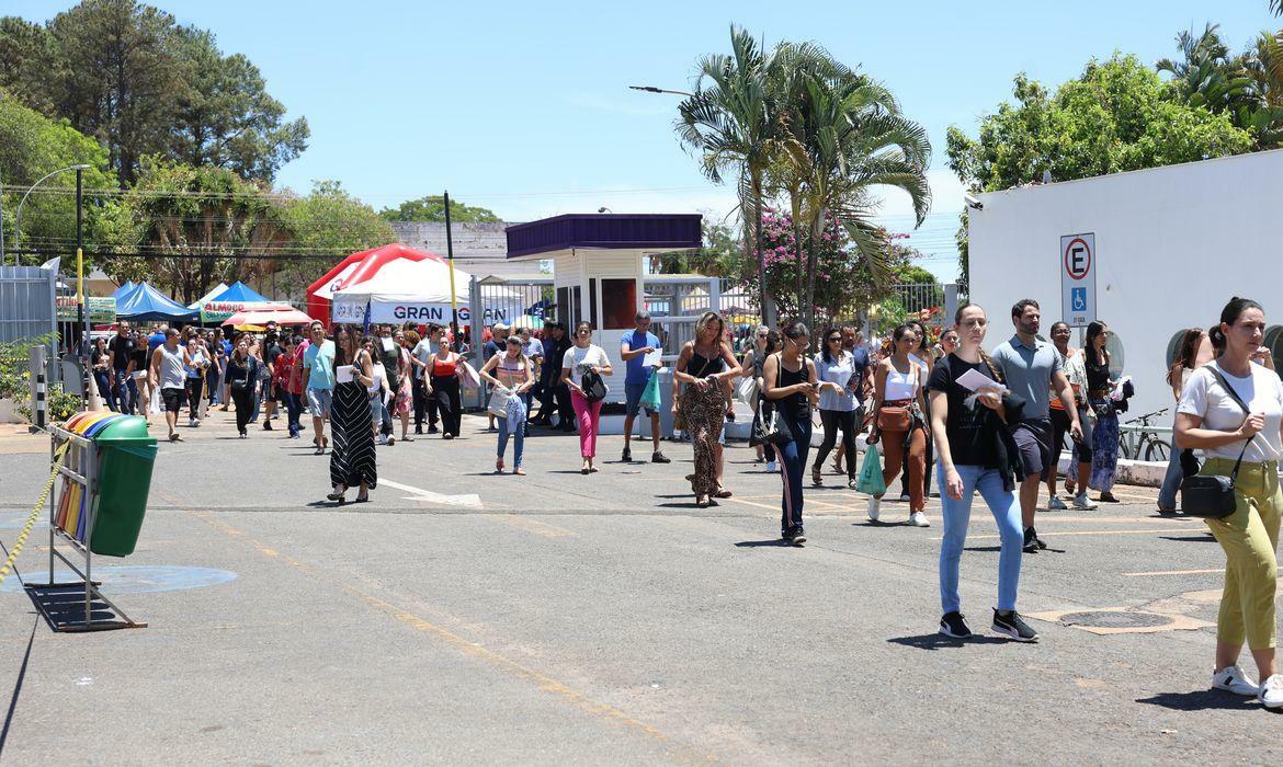 A imagem mostra candidatos caminhando para a realização de provas de um concurso público no Brasil