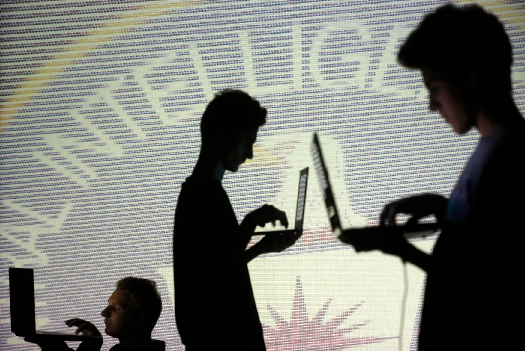 Silhueta de pessoas enquanto usam laptops em frente a uma imagem com códigos binários da Central Inteligence Agency (CIA)